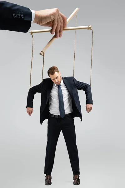 Vista recortada del titiritero sosteniendo marioneta de hombre de negocios en cuerdas aisladas en gris - foto de stock