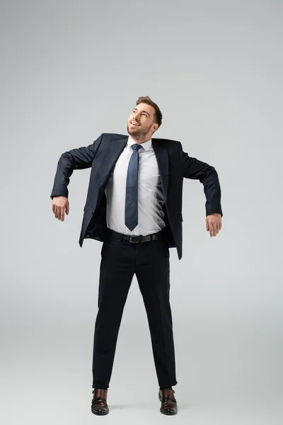 Heureux homme d'affaires marionnette en costume posant avec les mains vers le bas isolé sur gris — Photo de stock