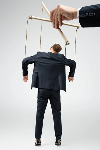 Cropped view of puppeteer holding businessman marionette on strings isolated on grey — Stock Photo