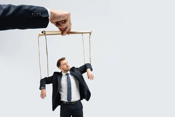 Vista recortada del titiritero sosteniendo marioneta de hombre de negocios en cuerdas aisladas en gris - foto de stock