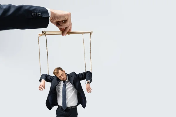 Vista recortada del titiritero sosteniendo marioneta de hombre de negocios en cuerdas aisladas en gris - foto de stock