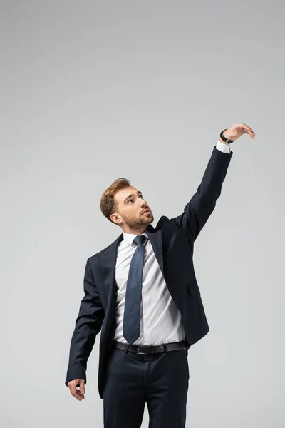 Hombre de negocios marioneta en traje con la mano levantada aislado en gris - foto de stock