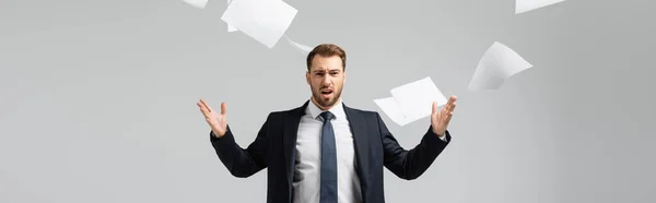 Недовольный бизнесмен в костюме бросает бумаги в воздух изолированные на сером, панорамный снимок — стоковое фото