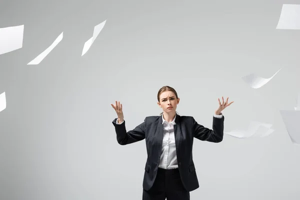 Donna d'affari scontenta in giacca e cravatta gettando carte in aria isolata su grigio — Stock Photo