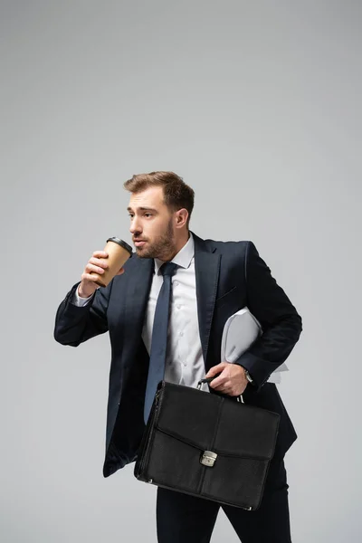 Бизнесмен с кожаным чемоданом и бумажной чашкой изолированы на сером — стоковое фото