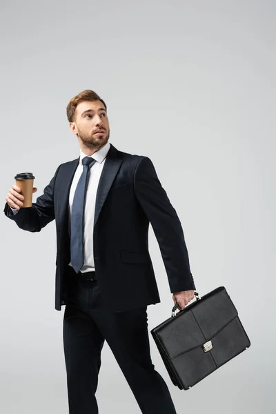 Homem de negócios com mala de couro e copo de papel olhando para longe isolado em cinza — Fotografia de Stock