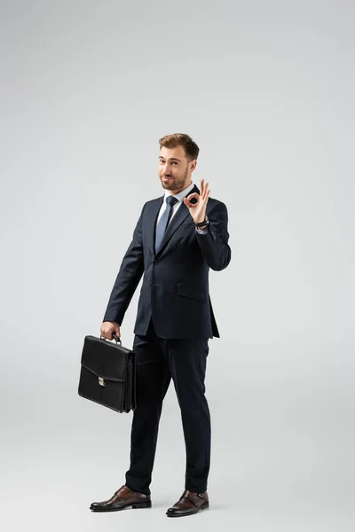 Businessman with leather suitcase showing ok sign isolated on grey — Stock Photo