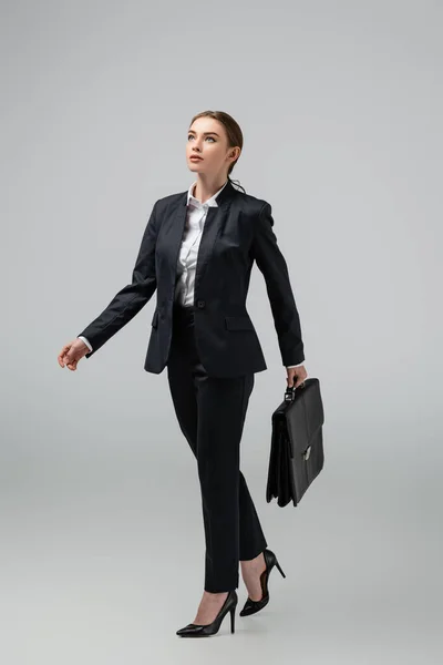 Jovem empresária andando com mala de couro isolado em cinza — Fotografia de Stock