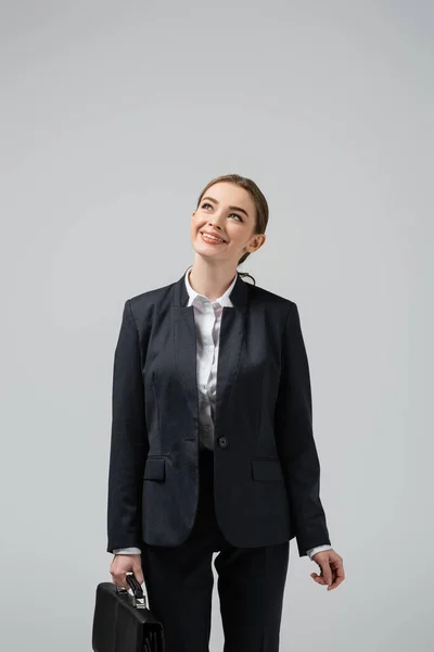 Sonriente joven mujer de negocios con maleta de cuero mirando hacia arriba aislado en gris - foto de stock