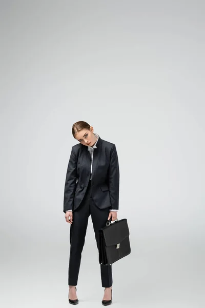 Triste joven empresaria con maleta de cuero aislada en gris — Stock Photo