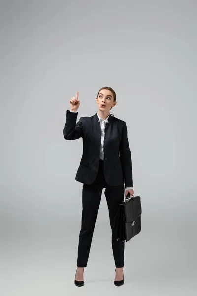 Young businesswoman with leather suitcase pointing up isolated on grey — Stock Photo