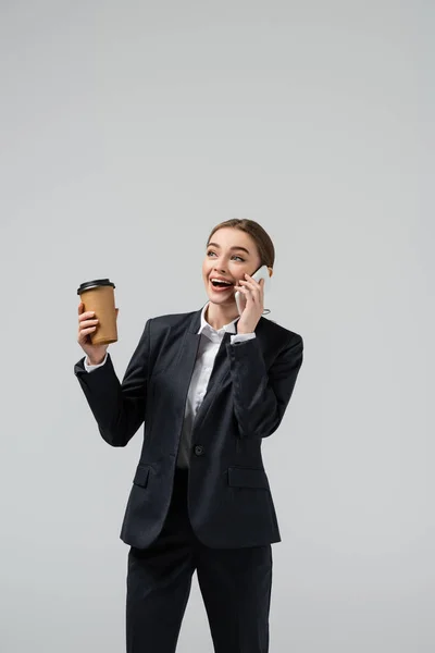 Feliz joven mujer de negocios con café para ir a hablar en el teléfono inteligente aislado en gris - foto de stock