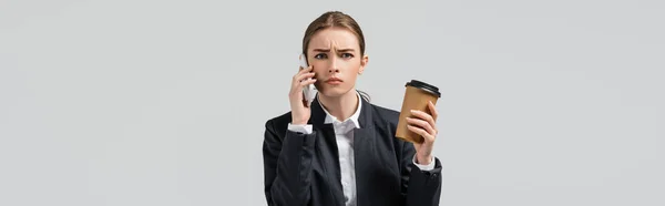 Jeune femme d'affaires confus avec du café pour aller parler sur smartphone isolé sur gris, prise de vue panoramique — Photo de stock