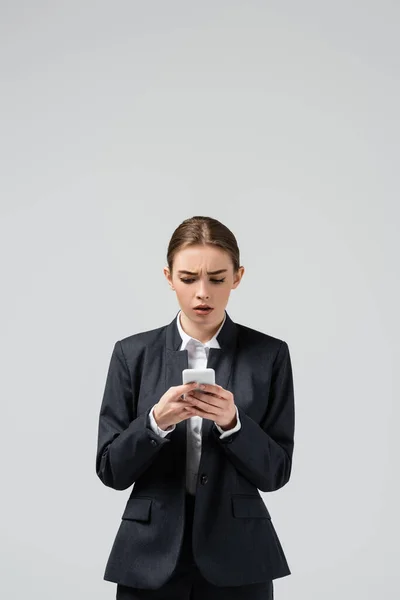 Confused young businesswoman using smartphone isolated on grey — Stock Photo