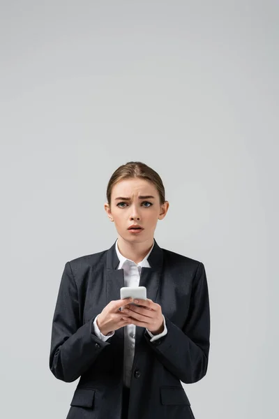 Traurige junge Geschäftsfrau nutzt Smartphone isoliert auf grau — Stockfoto