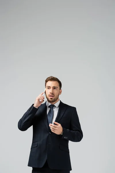 Embarrassed handsome businessman in suit talking on smartphone isolated on grey — Stock Photo
