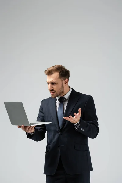 Angry handsome businessman in suit using laptop isolated on grey — Stock Photo