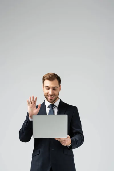 Sorridente bonito empresário em terno ter vídeo chat no laptop isolado em cinza — Fotografia de Stock