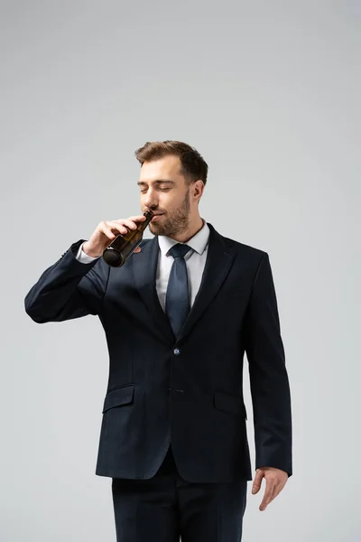 Guapo hombre de negocios en traje bebiendo cerveza aislado en gris - foto de stock