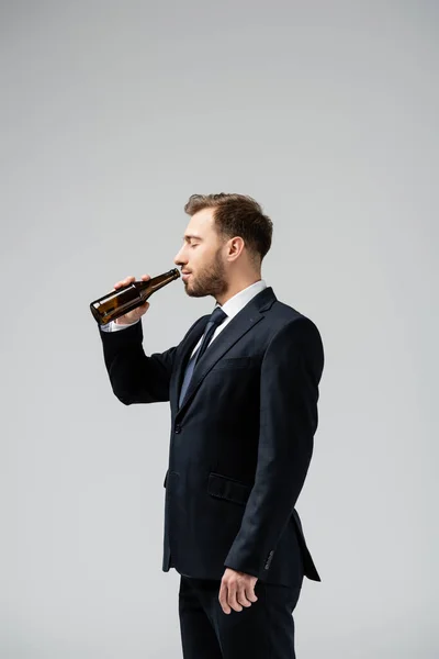 Side view of handsome businessman in suit drinking beer isolated on grey — Stock Photo