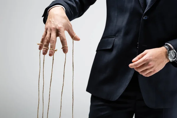 Partial view of puppeteer in suit with strings on fingers isolated on grey — Stock Photo