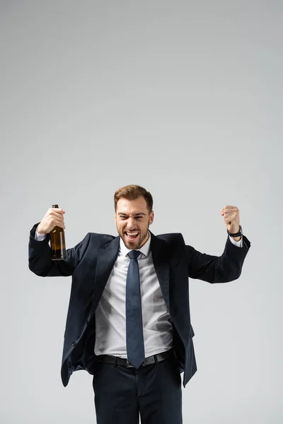 Guapo hombre de negocios en traje regocijándose con cerveza aislada en gris - foto de stock