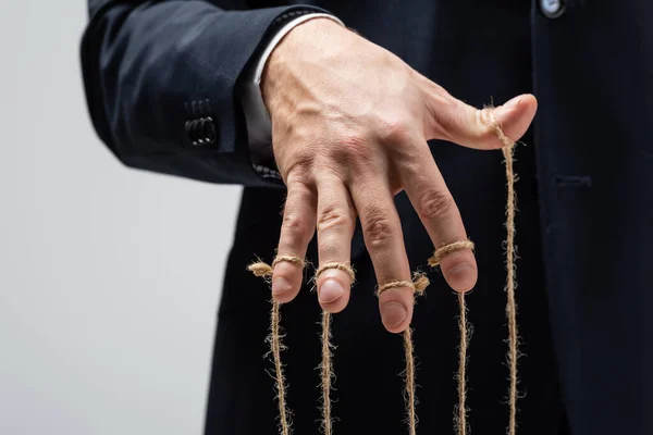 Partial view of puppeteer in suit with strings on fingers isolated on grey — Stock Photo