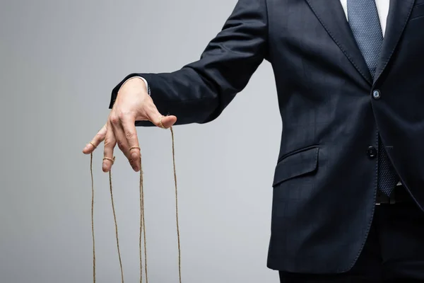 Partial view of puppeteer in suit with strings on fingers isolated on grey — Stock Photo