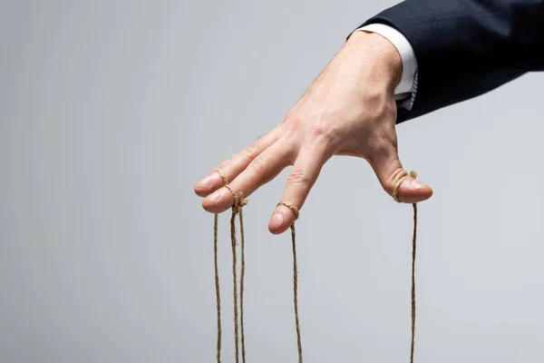 Partial view of puppeteer in suit with strings on fingers isolated on grey — Stock Photo