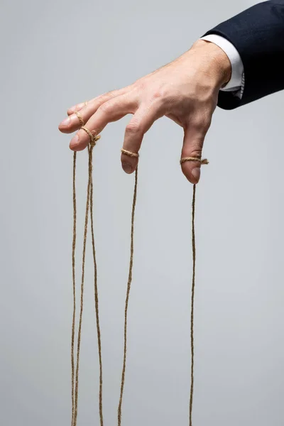 Partial view of puppeteer in suit with strings on fingers isolated on grey — Stock Photo