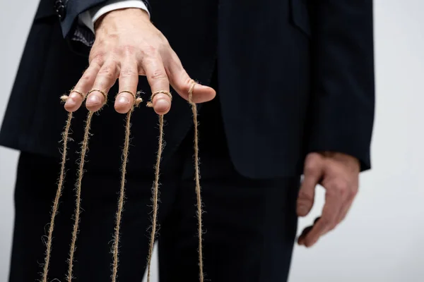 Vista parcial del titiritero en traje con cuerdas en los dedos aislados en gris - foto de stock