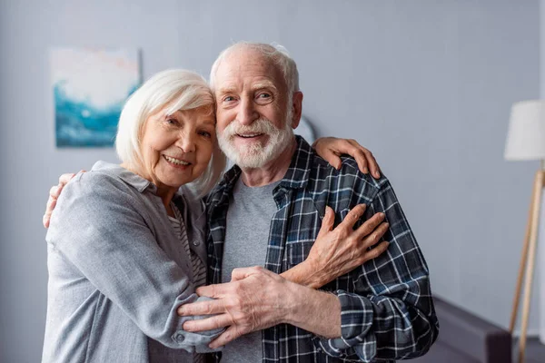 Glückliches Seniorenpaar lächelt und umarmt, während es in die Kamera blickt — Stockfoto