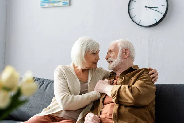 Enfoque selectivo de la feliz pareja de ancianos sentados en el sofá y mirándose entre sí - foto de stock
