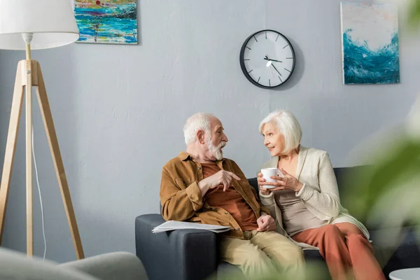 Selective focus of happy senior couple talking while sitting on sofa at home — Stock Photo