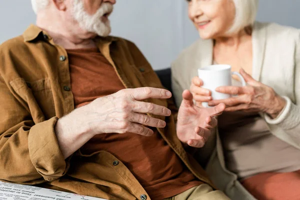 Enfoque selectivo de hombre mayor gesto mientras habla sonriente esposa sosteniendo taza de té — Stock Photo