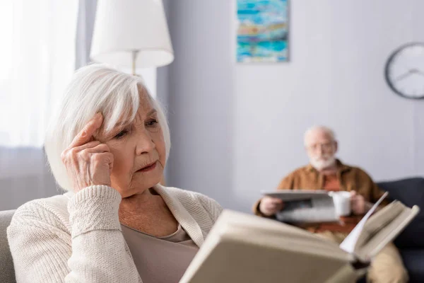 Foyer sélectif de la femme âgée attentive lecture livre près du mari avec journal sur fond — Photo de stock