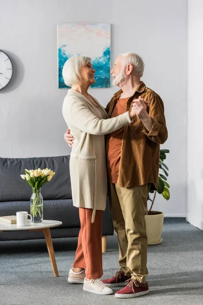 Heureux couple de personnes âgées dansant tout en se regardant près de la table avec des tulipes — Photo de stock