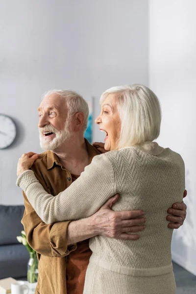 Feliz pareja de ancianos bailando, riendo y mirando hacia otro lado en casa - foto de stock