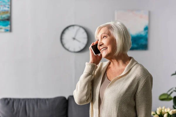 Glückliche Seniorin lächelt und schaut weg, während sie mit dem Smartphone spricht — Stockfoto