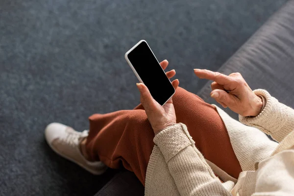 Vista de ángulo alto de la mujer mayor sosteniendo teléfono inteligente con pantalla en blanco - foto de stock