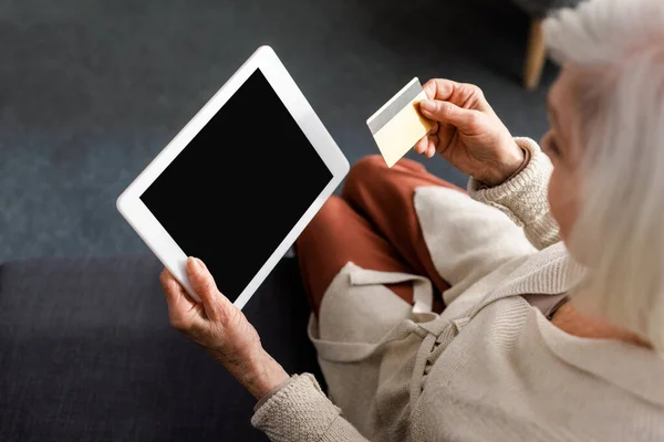 Partial view of senior woman holding digital tablet with blank screen and credit card, overhead view — Stock Photo