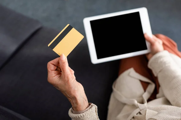 Cropped view of senior woman holding digital tablet with blank screen and credit card, top view — Stock Photo
