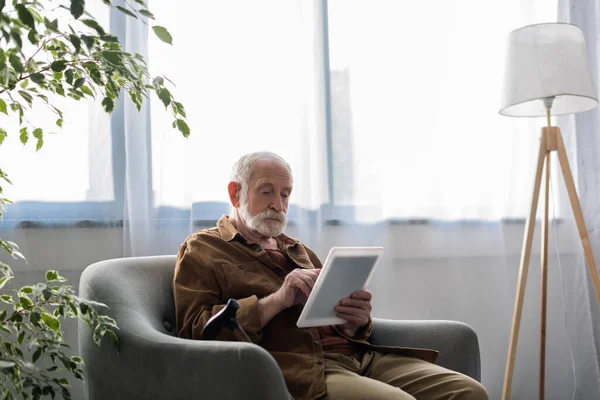 Hombre mayor concentrado usando tableta digital mientras está sentado en el sillón - foto de stock