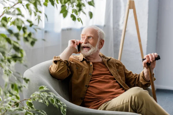 Enfoque selectivo de hombre mayor feliz sentado en el sillón y hablando en el teléfono inteligente - foto de stock