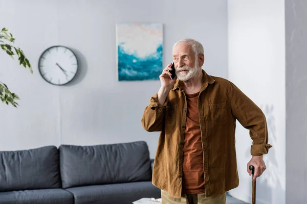 Aufmerksame Seniorin spricht mit Smartphone im Stehen mit Gehstock — Stockfoto