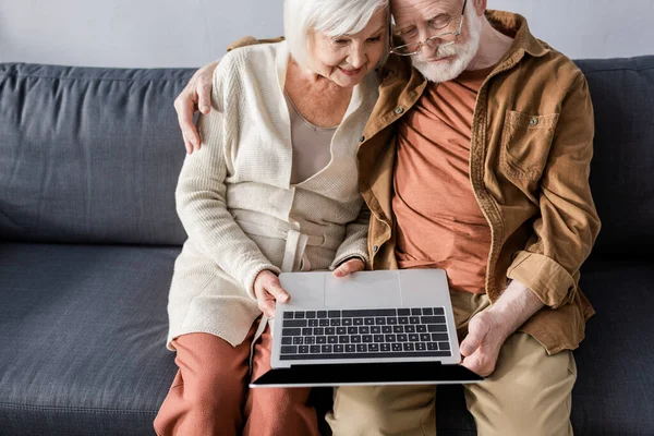 Высокий угол обзора счастливой пожилой пары, сидящей на диване и с помощью ноутбука — стоковое фото