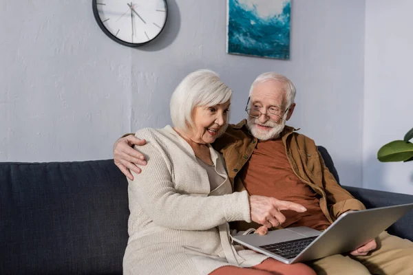 Hombre mayor abrazando esposa excitada señalando con el dedo a la computadora portátil - foto de stock