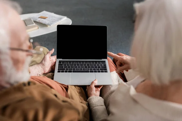 Selective focus of senior couple using laptop with blank screen, overhead view — Stock Photo
