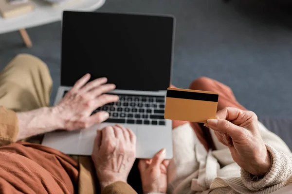 Vista recortada del hombre mayor utilizando aptop con pantalla en blanco cerca de la esposa celebración de la tarjeta de crédito, vista superior - foto de stock