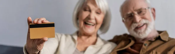 Messa a fuoco selettiva di allegra donna anziana mostrando carta di credito vicino uomo sorridente, intestazione del sito web — Foto stock